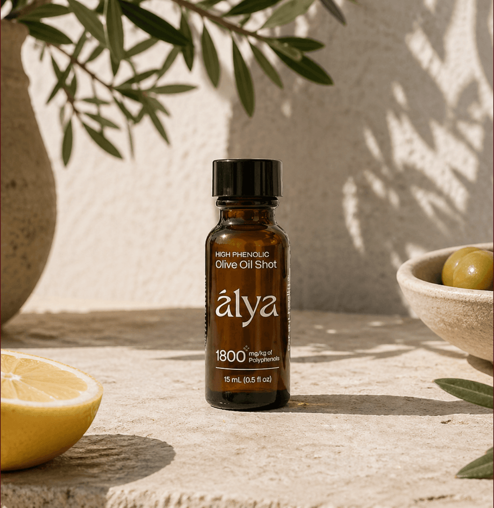 An Alya olive oil shot bottle on sunlit stone beside a lemon